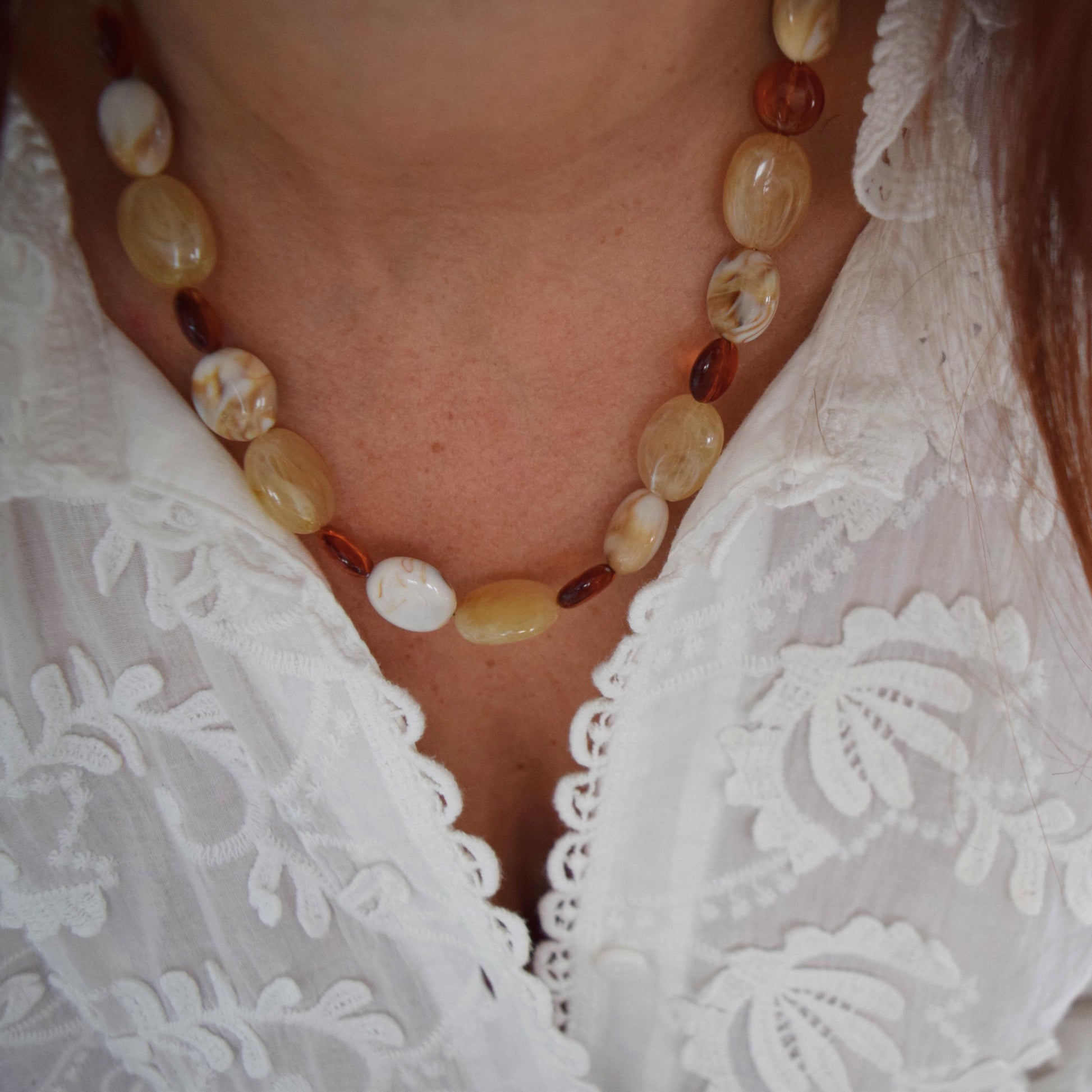 Collier en perles beige et cuivrées porté sur un chemisier blanc