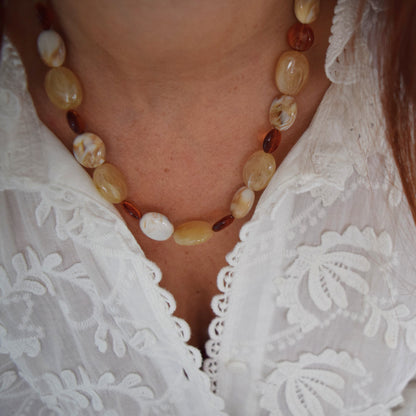 Collier en perles beige et cuivrées porté sur un chemisier blanc