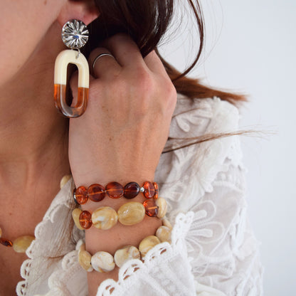 Détail du pendentif en résine ambrée et crème, finition brillante et forme géométrique ovale.