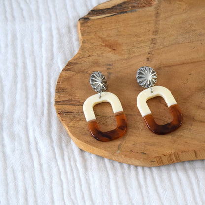 Détail du pendentif en résine ambrée et crème, finition brillante et forme géométrique ovale.