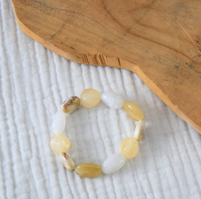 Vue rapprochée du bracelet en perles beige et blanches sur fond bois.