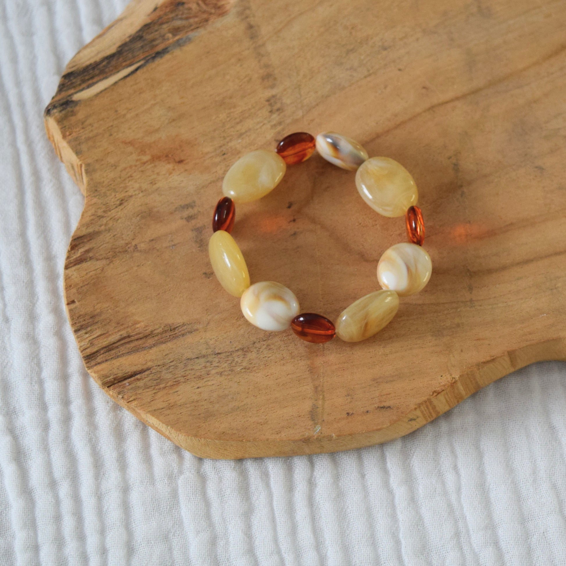 Détail du bracelet SIENNA en perles beige et cuivrées sur fond bois naturel.