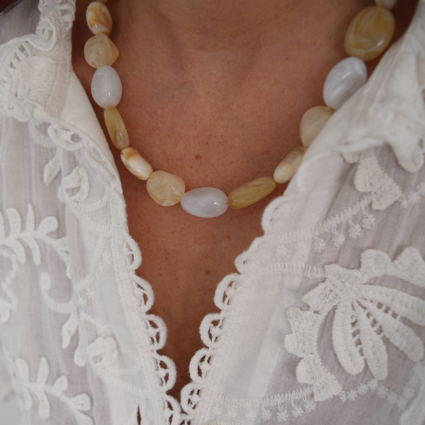 Collier fait main en perles blanches et beige porté au cou